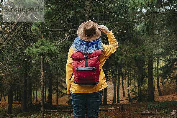 Frau berührt Hut und schaut auf Bäume im Wald