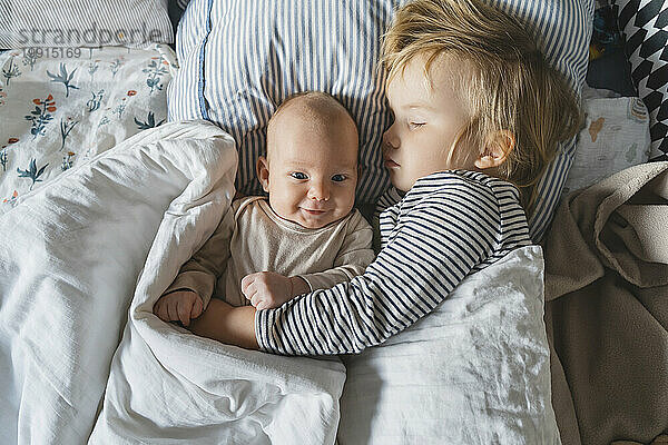 Lächelnder kleiner Junge neben seiner Schwester  die zu Hause im Bett schläft