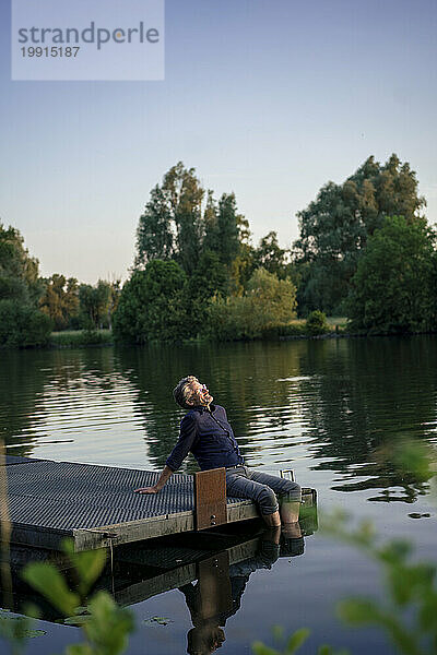 Mann sitzt bei Sonnenuntergang auf einem Steg in der Nähe des Sees