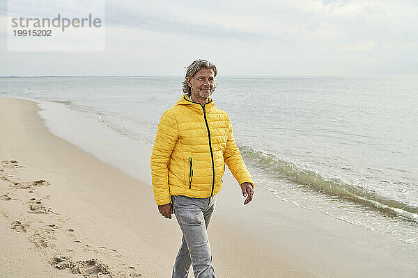 Lächelnder älterer Mann  der am Strand spaziert
