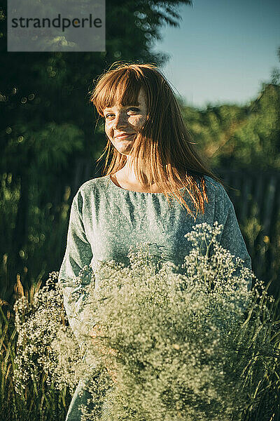 Lächelnde rothaarige junge Frau mit Blumen an einem sonnigen Tag