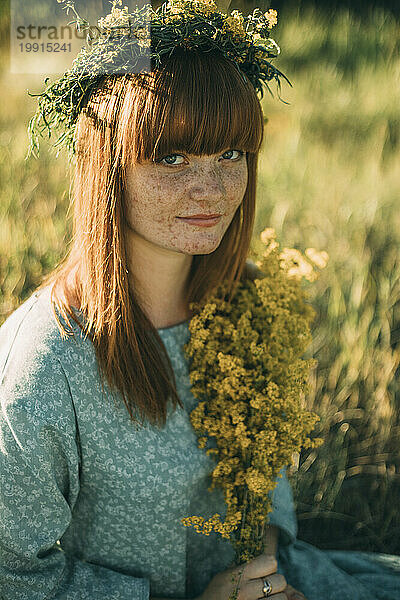 Junge rothaarige Frau trägt einen Blumenkranz auf dem Feld