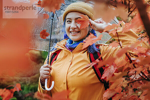 Lächelnde Frau hält Blatt über Gesicht im Herbstpark