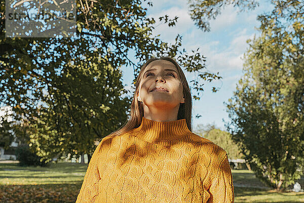 Lächelnde Frau mit orangefarbenem Pullover im Herbstpark