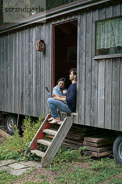 Freiberufler sitzt mit Frau im Türrahmen einer Blockhütte