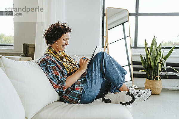 Lächelnder Illustrator mit Grafiktablett  der auf dem Sofa im Büro sitzt