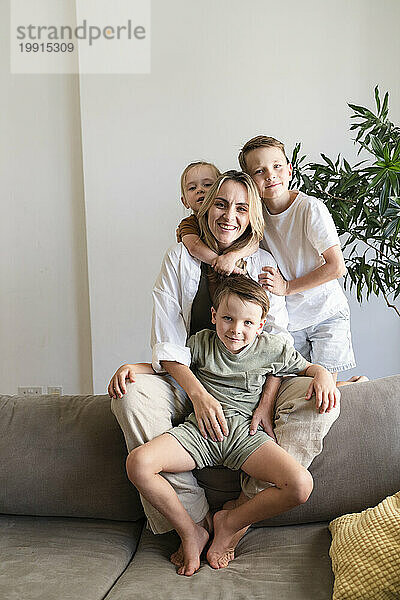 Lächelnde Mutter mit drei Söhnen  die zu Hause auf dem Sofa sitzen