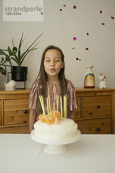 Glückliches Mädchen  das zu Hause Kerzen auf Geburtstagstorte bläst