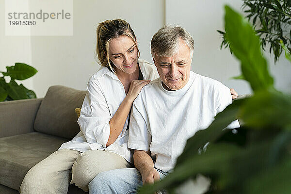 Smiling woman and senior man sitting on sofa at home