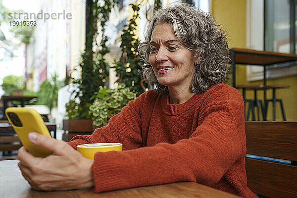 Glückliche reife Frau benutzt Smartphone mit Kaffeetasse auf dem Tisch im Straßencafé