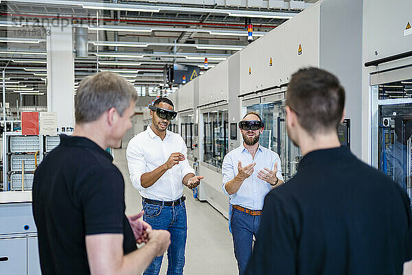Kollegen beobachten zwei Techniker mit Augmented-Reality-Brillen in einer Fabrik