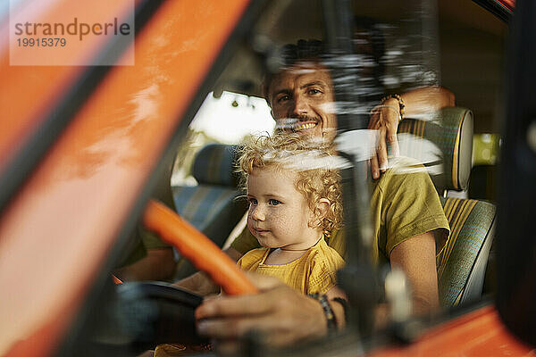 Smiling father sitting with daughter on driver's seat of caravan