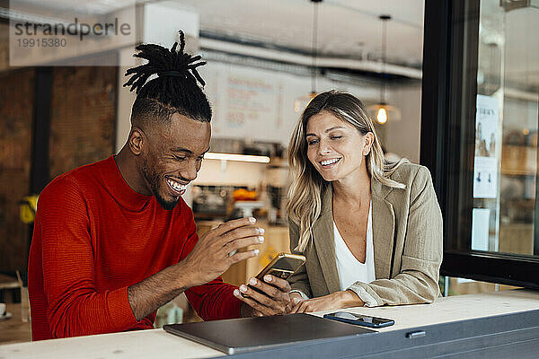 Glückliche Kollegin nutzt Smartphone von Geschäftsfrau im Café