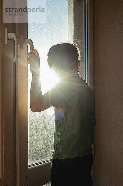 Junge schaut an einem sonnigen Tag durch das Fenster