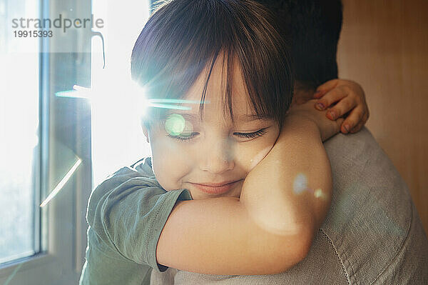 Smiling boy hugging father near window at home