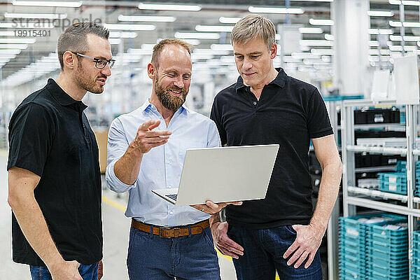 Geschäftsmann teilt Laptop mit Mitarbeitern in einer Fabrik