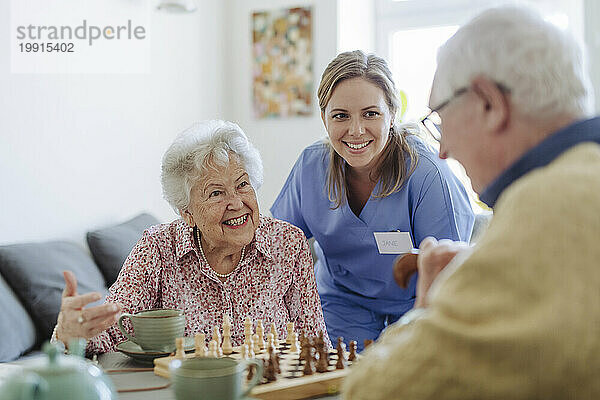 Glückliche medizinische Fachkraft mit älterem Paar  das Schach spielt