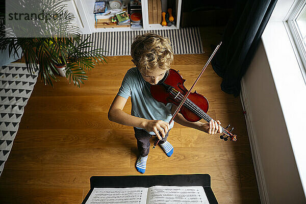 Junge mit blonden Haaren übt zu Hause Geige vor Noten