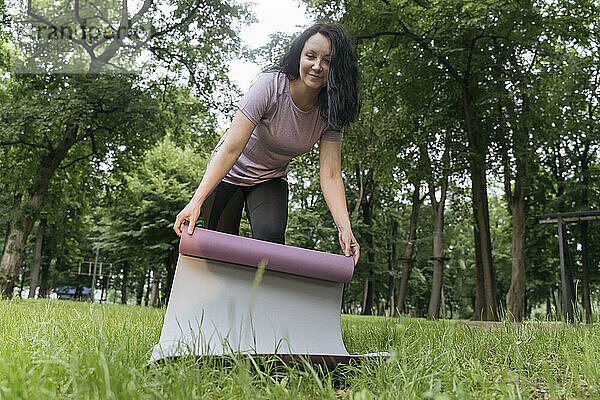 Frau legt Gymnastikmatte auf Gras im Park