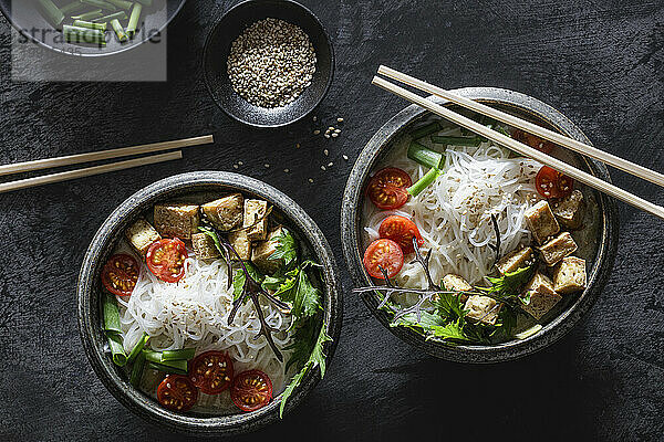 Bowls of vegan Tom kha kai soup with tofu  tomatoes  salad  rice noodles  sesame seeds and scallion
