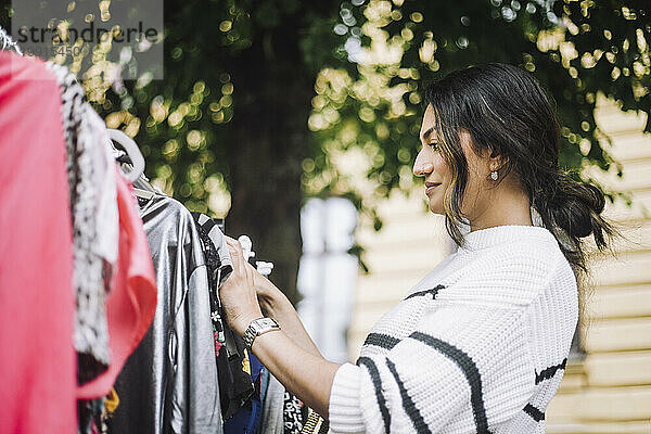 Seitenansicht einer lächelnden Frau  die auf einem Flohmarkt ein Kleid kauft