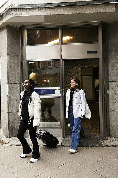 Lächelnde Freundinnen verlassen das Hotel mit Gepäck