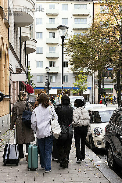 Rückansicht junger weiblicher Touristenfreunde  die mit Gepäck auf dem Bürgersteig in der Stadt spazieren