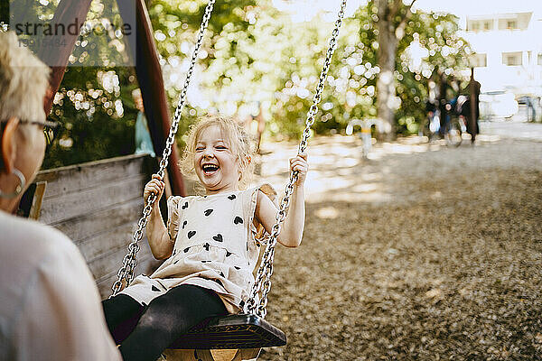 Fröhliches Mädchen lacht  während es mit Großmutter im Park auf der Schaukel spielt
