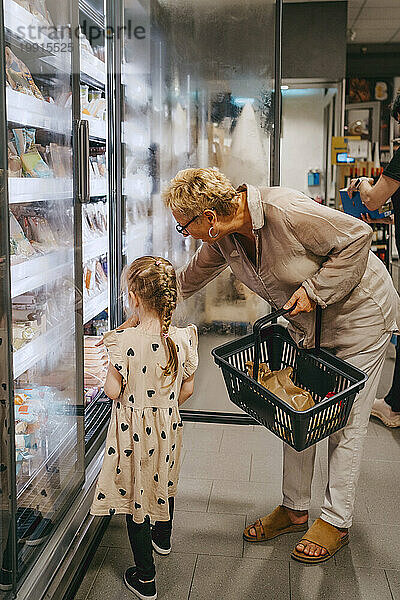 Mädchen kauft mit Großmutter im Supermarkt Tiefkühlkost aus dem Kühlregal