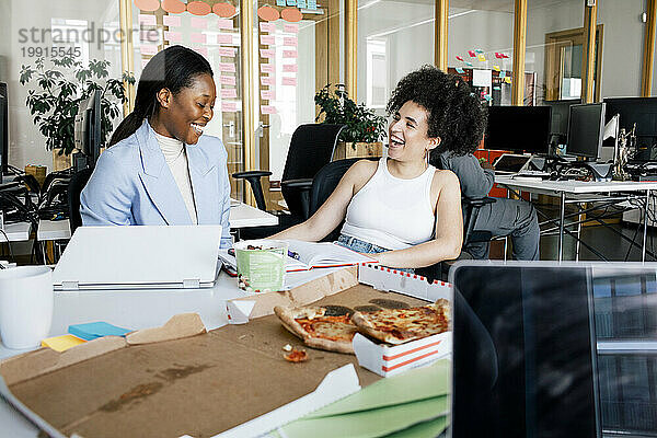 Glückliche Geschäftsfrauen lachen  während sie im Büro sitzen