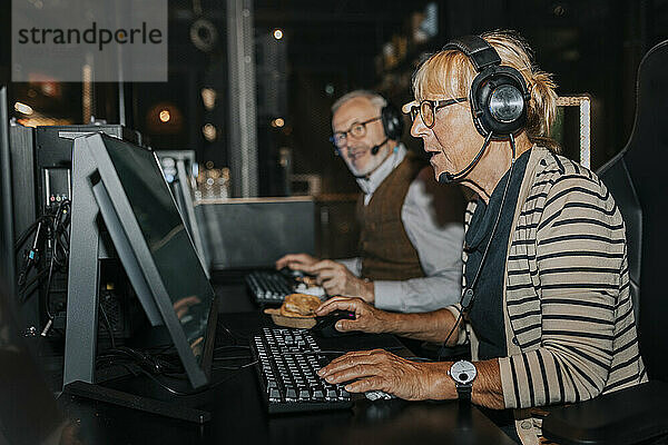 Ältere Frau spielt Videospiel am Computer von einem männlichen Freund im Gaming-Center
