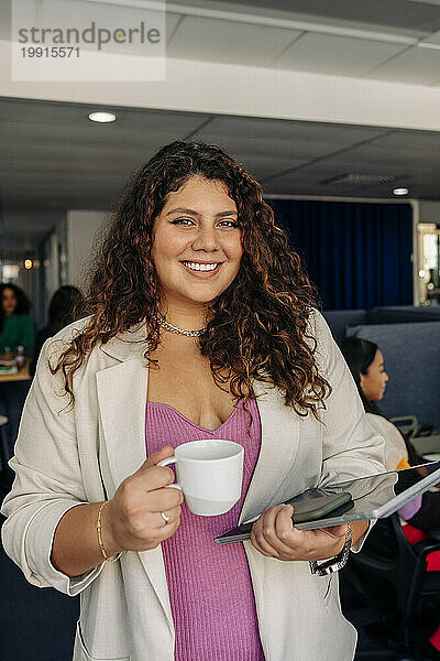 Porträt einer lächelnden jungen Geschäftsfrau mit Kaffeetasse im Büro