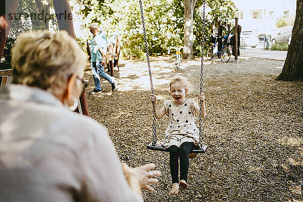 Fröhliches Mädchen spielt mit Großmutter im Park auf Schaukel