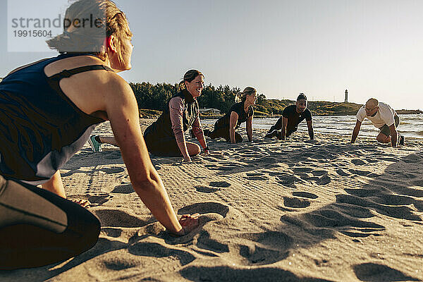 Lächelnde Trainerin beim Stretching mit Team im Sand am Strand
