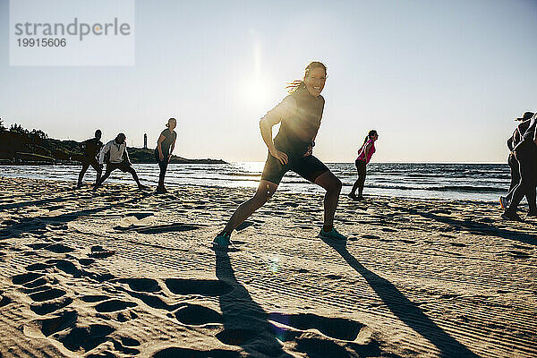 Glückliche Frau trainiert mit ihrem Team während einer Gruppentrainingseinheit am Strand