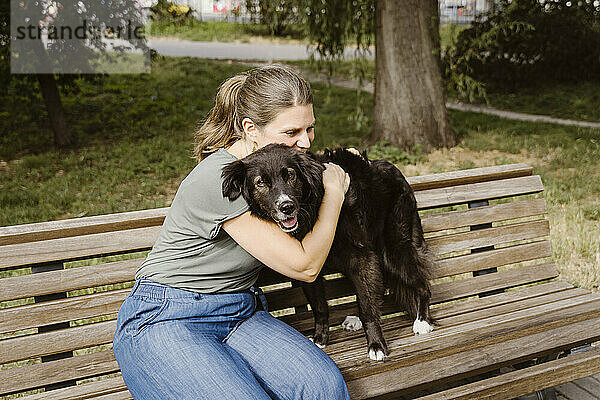 Reife Frau umarmt Hund auf Bank im Park