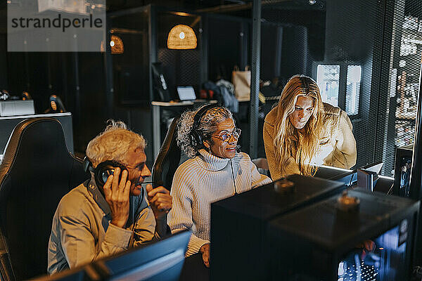 Frau hilft älterem Paar am Wochenende beim Computerspiel in der Gaming-Lounge