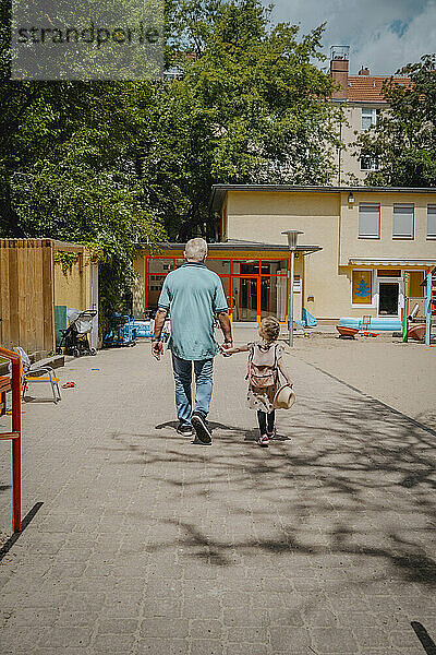 Großvater und Enkelin gehen auf Fußweg in Richtung Kindergarten