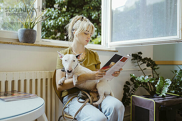Frau mit Hund liest Zeitschrift  während sie im Wartezimmer einer Tierklinik sitzt