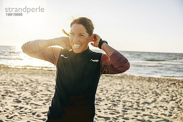Fröhliche Trainerin lacht  während sie am Strand steht