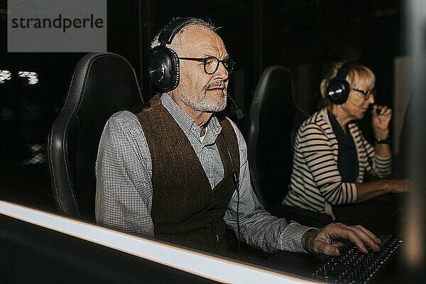 Älterer Mann mit Headset spielt von einer Freundin im Gaming-Center ein Videospiel am Computer