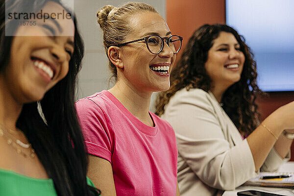 Glückliche Geschäftsfrauen lachen mit Kolleginnen während eines Treffens im Büro
