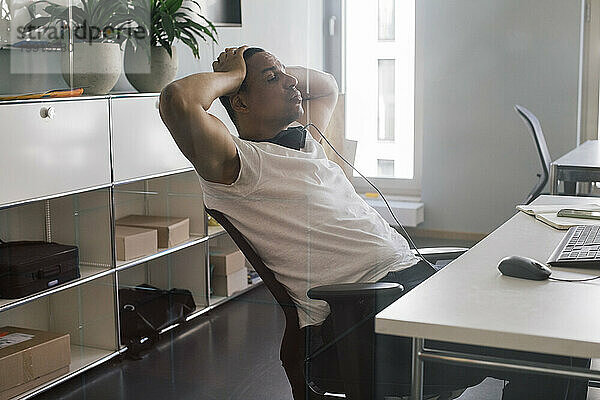 Überarbeiteter männlicher Unternehmer sitzt mit dem Kopf in der Hand auf einem Stuhl im Büro