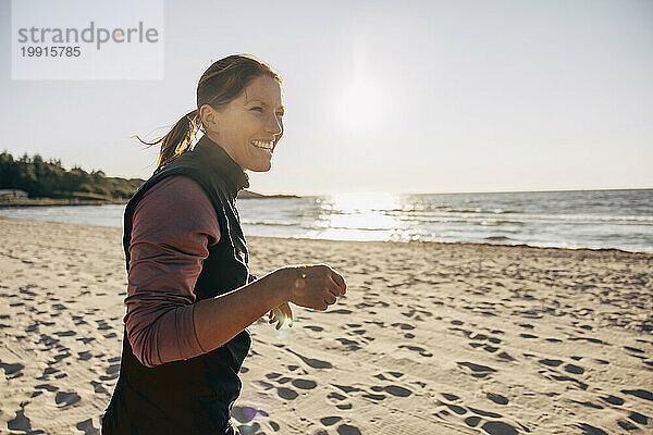 Seitenansicht einer glücklichen reifen Frau am Strand an einem sonnigen Tag