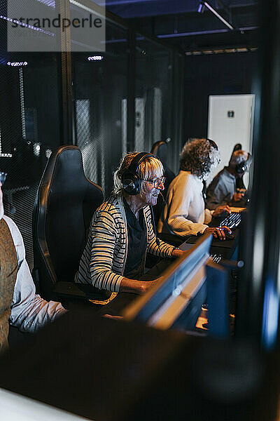 Multiracial elderly male and female friends playing game on computers in gaming center