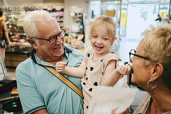 Fröhliches Mädchen  das Spaß mit Großmutter beim Einkaufen im Supermarkt hat