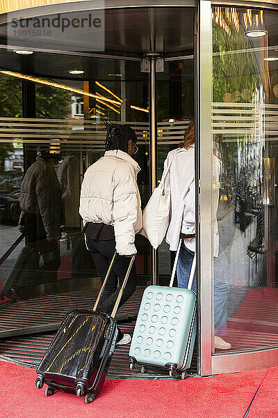 Junge weibliche Touristen mit Rollgepäck betreten das Hotel durch die Drehtür