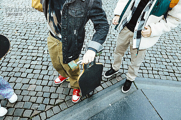 Unterer Teil eines Jungen mit Skateboard  der neben seinem männlichen Freund auf dem Fußweg steht