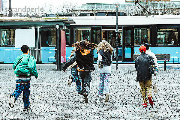 Rückansicht männlicher und weiblicher Freunde  die in der Stadt auf die Straßenbahn zulaufen