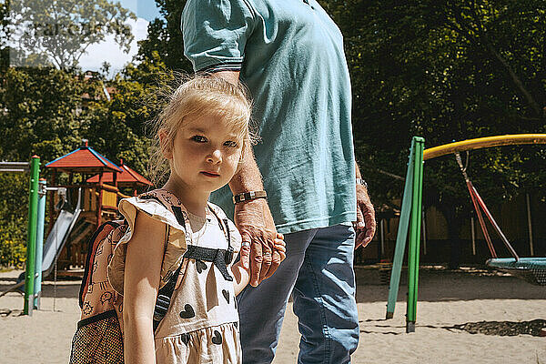 Porträt eines Mädchens  das Händchen hält  während es mit seinem Großvater im Kindergarten steht